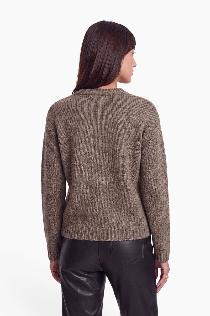 Eine Frau, von hinten gesehen, trägt einen braunen, langärmeligen Pullover aus einer Mohairmischung mit Rundhalsausschnitt. Dazu trägt sie eine schwarze Hose im Lederlook.