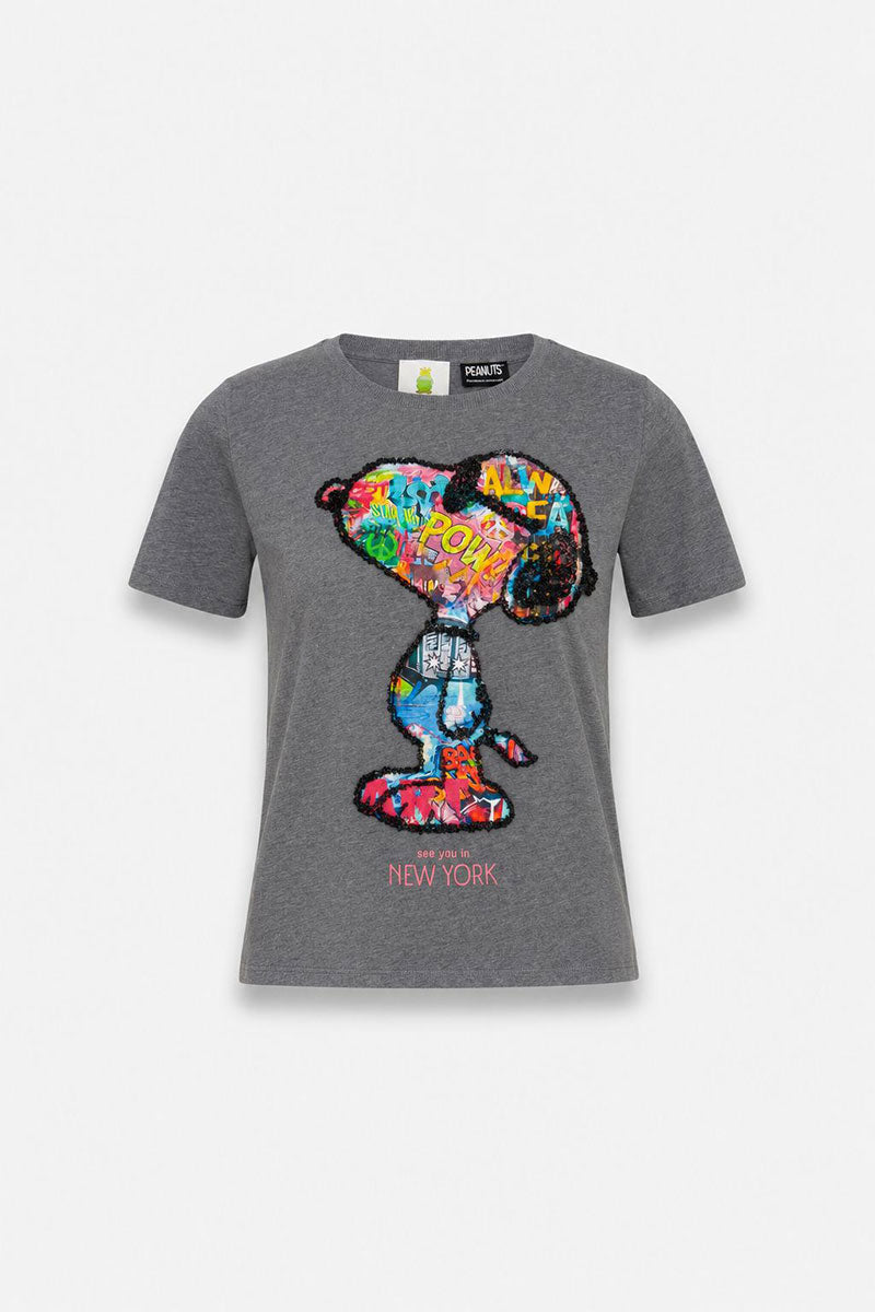 Graues Snoopy-T-Shirt mit kurzen Ärmeln und einem farbenfrohen Snoopy-Motiv im Pop-Art-Stil mit Pailletten im Comic-Look. Unterhalb von Snoopy ist in rosa Schrift „NEW YORK“ zu lesen. Das Shirt besteht aus 100 % Baumwolle und liegt flach auf einem einfarbigen, hellen Hintergrund, sodass das Motiv auf der Vorderseite deutlich zu erkennen ist.