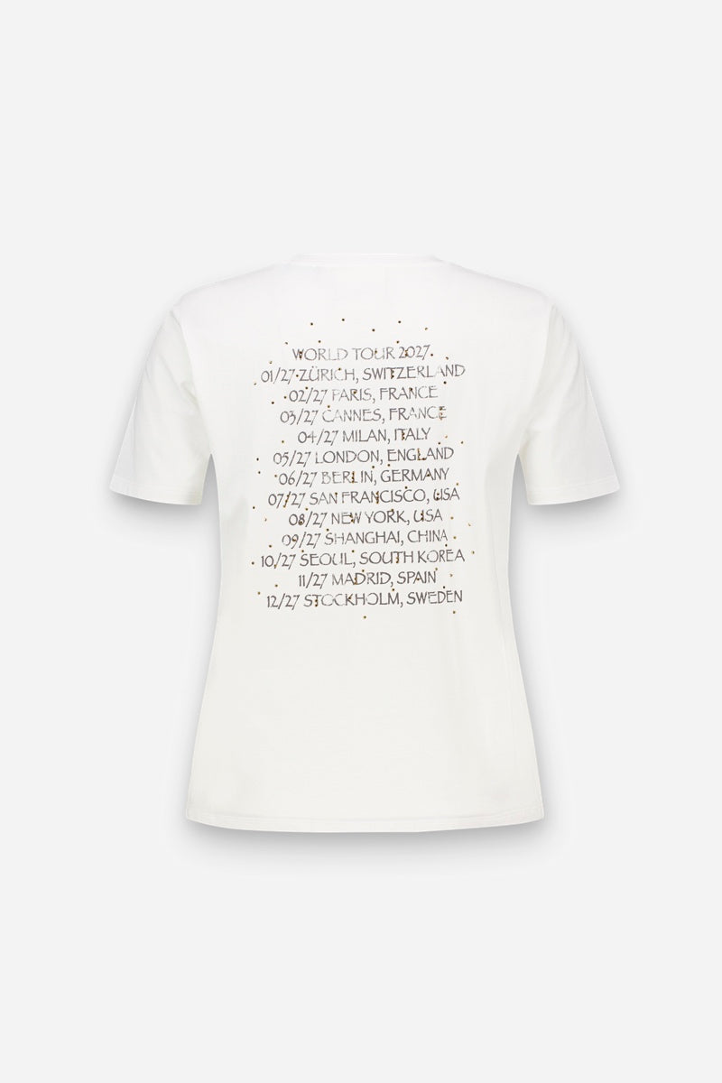 Die Rückseite eines weißen Snoopy-T-Shirts aus Baumwolle mit einem „World Tour 2027“-Motiv. Der Text listet zwölf Städte und Termine auf, die von Zürich bis Stockholm reichen, umgeben von einem dezenten, gepunkteten kreisförmigen Rand, der mit Strasssteinen verziert ist.