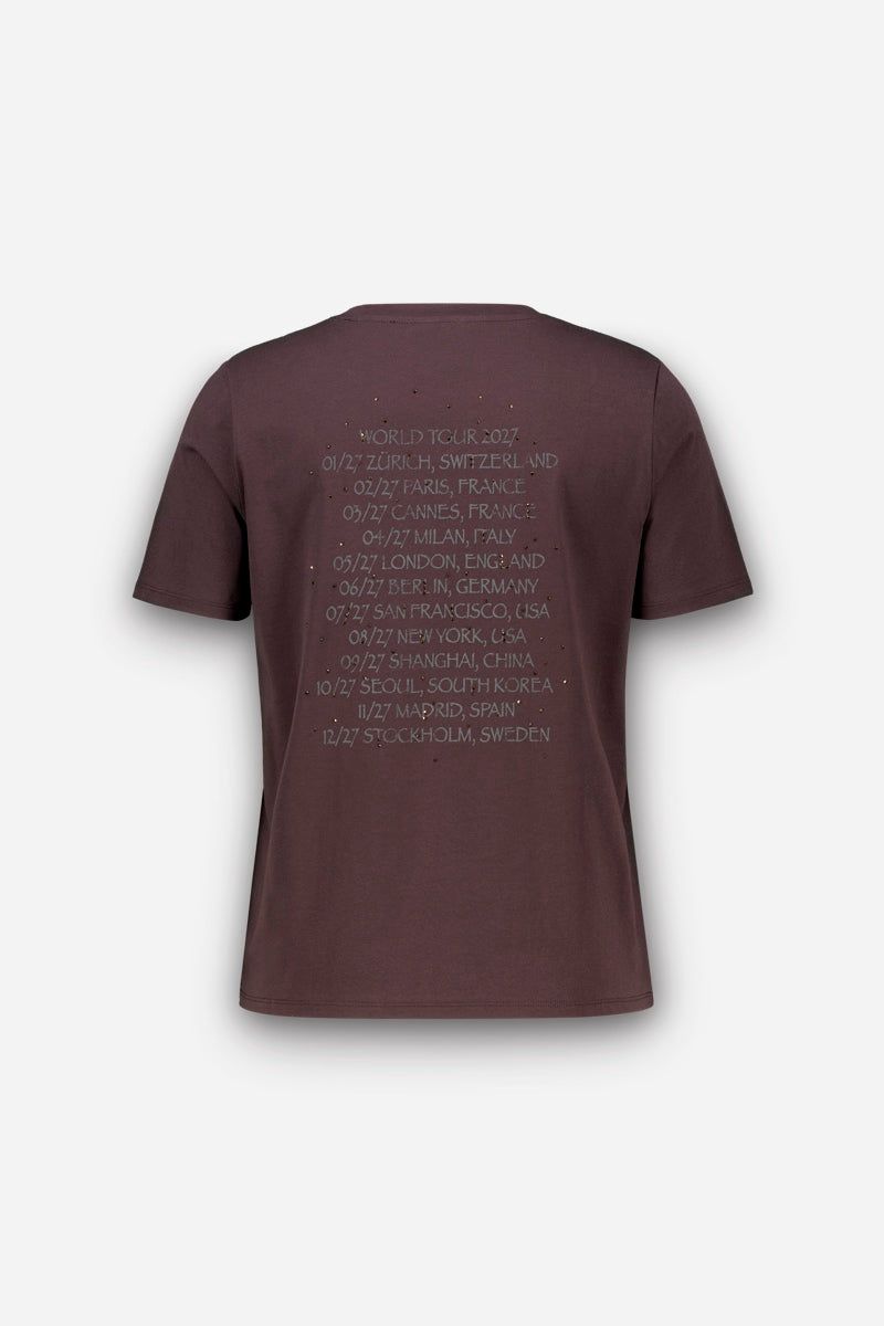 Auf der Rückseite eines braunen Snoopy-T-Shirts aus Baumwolle ist eine Liste der Städte und Termine der „World Tour 2027“ in einer Used-Schriftart aufgedruckt. Der Text enthält Orte wie Zürich, Paris, Mailand, London, Berlin, San Francisco, New York, Shanghai, Seoul, Madrid und Stockholm.