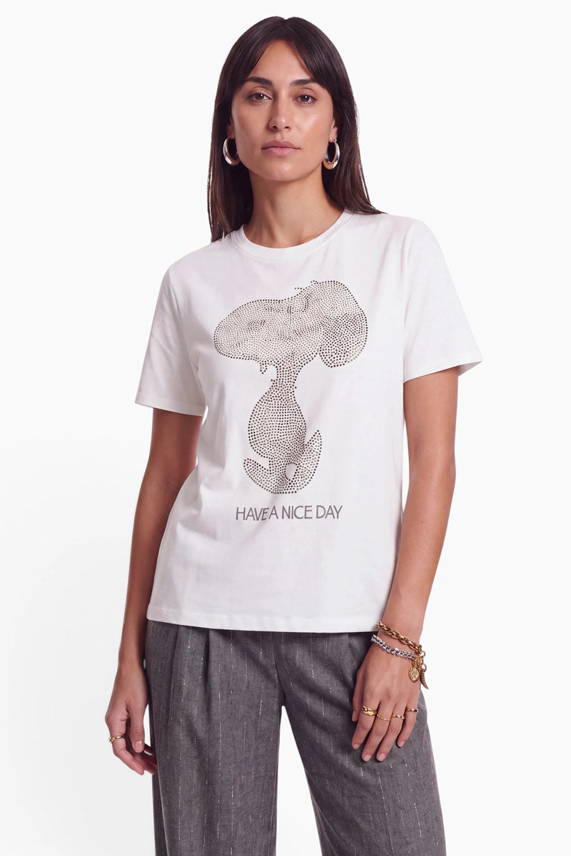 Eine Frau trägt ein weißes Snoopy-T-Shirt aus Baumwolle mit einer stilisierten Figurengrafik aus kleinen Nieten. Unterhalb der Figur ist der Schriftzug „HAVE A NICE DAY“ in schlichter schwarzer Schrift aufgedruckt.