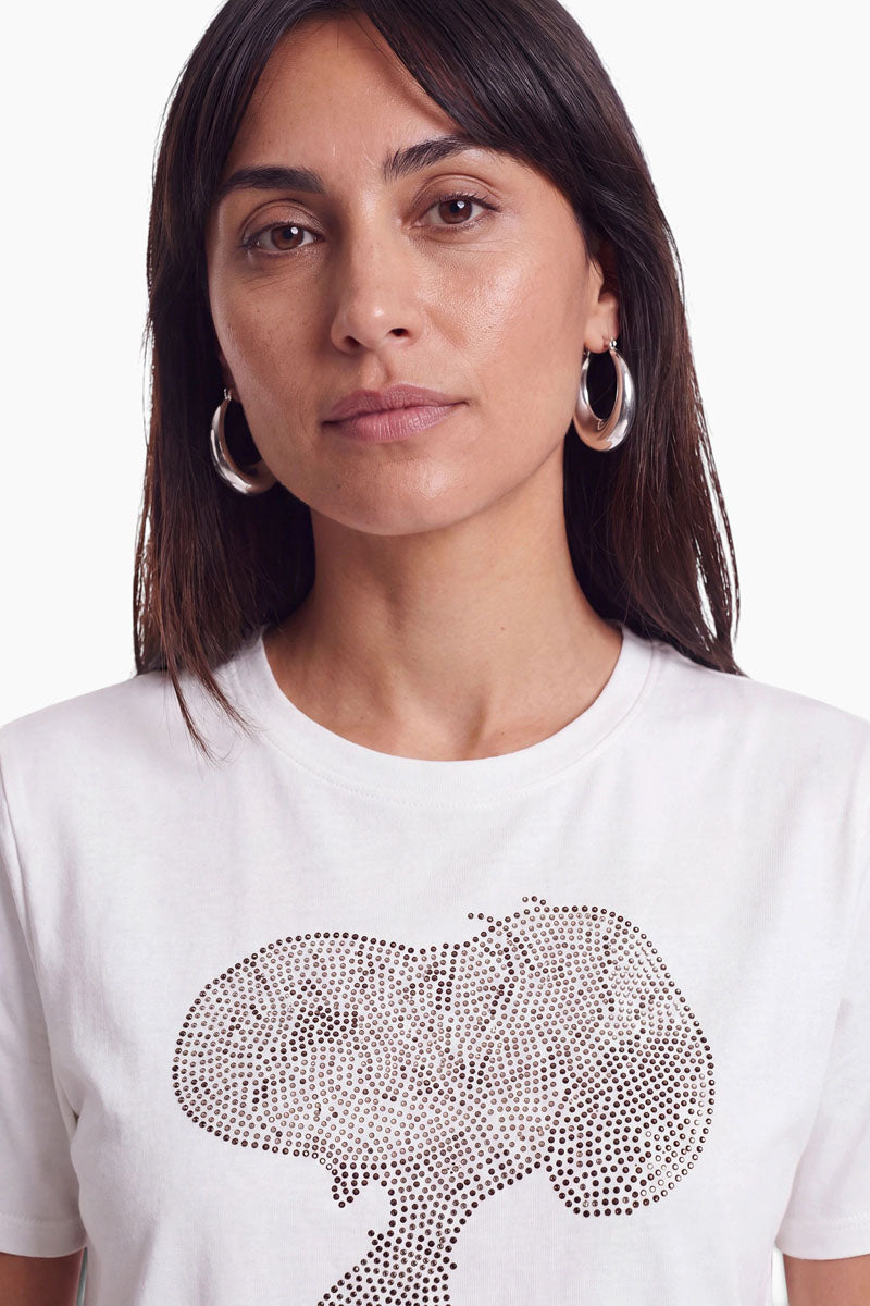 Ein Nahaufnahme-Porträt einer Frau, die silberne Creolen und ein weißes Snoopy-T-Shirt aus Baumwolle trägt, auf dem ein Motiv aus kleinen dunklen Strasssteinen aufgebracht ist.