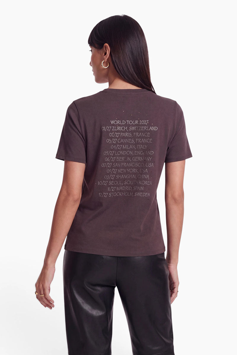Eine Person, von hinten gesehen, die ein dunkelbraunes Snoopy-T-Shirt trägt, auf dem „World Tour 2027“ sowie eine Liste internationaler Städte und Termine in weißer Schrift aufgedruckt sind.