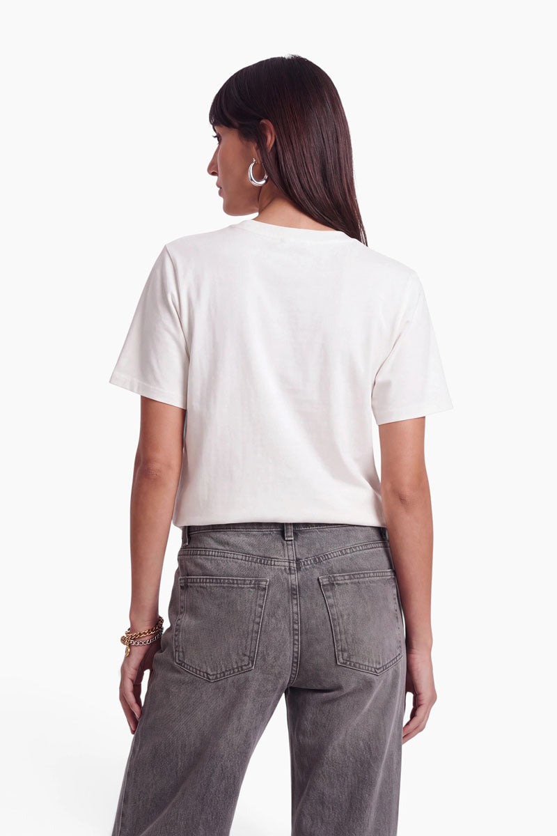 Eine Person, von hinten gesehen, die ein weißes „Peanuts“-T-Shirt und eine graue Jeans trägt.