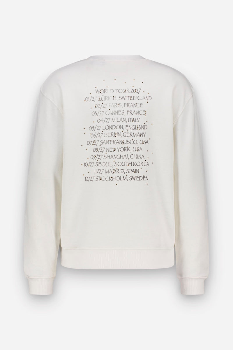 Auf der Rückseite eines cremefarbenen Baumwoll-Sweatshirts ist eine Liste der Termine und Veranstaltungsorte der Welttournee 2027 im Snoopy-Design aufgedruckt, darunter Städte wie Zürich, Paris, London und Seoul.
