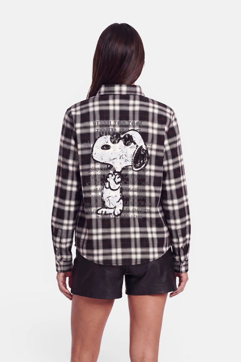 Eine Person, die eine schwarz-weiße Karoprint-Hemdbluse mit einem großen Snoopy-Aufdruck auf dem Rücken trägt, dazu schwarze Shorts. Die Person ist von hinten vor einem weißen Hintergrund zu sehen.