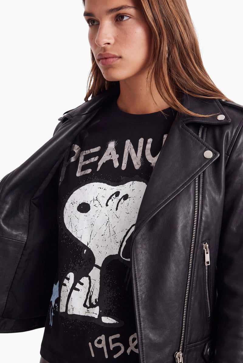 Eine Person mit langen braunen Haaren trägt eine schwarze Leder-Motorradjacke über einem Snoopy-T-Shirt aus Baumwolle im Used-Look mit dem Peanuts 1950-Logo.