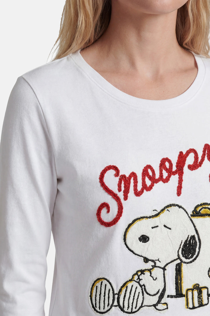 Eine Frau mit hellem, gewelltem Haar trägt ein limitiertes „Princess Goes Hollywood“-Snoopy-Shirt aus Baumwolle, auf dem Snoopy auf seiner Hundehütte gestickt ist und der Schriftzug „Snoopy“ in großen roten Kursivbuchstaben zu sehen ist. Nur ihr Oberkörper und ein Teil ihres Gesichts sind zu sehen.