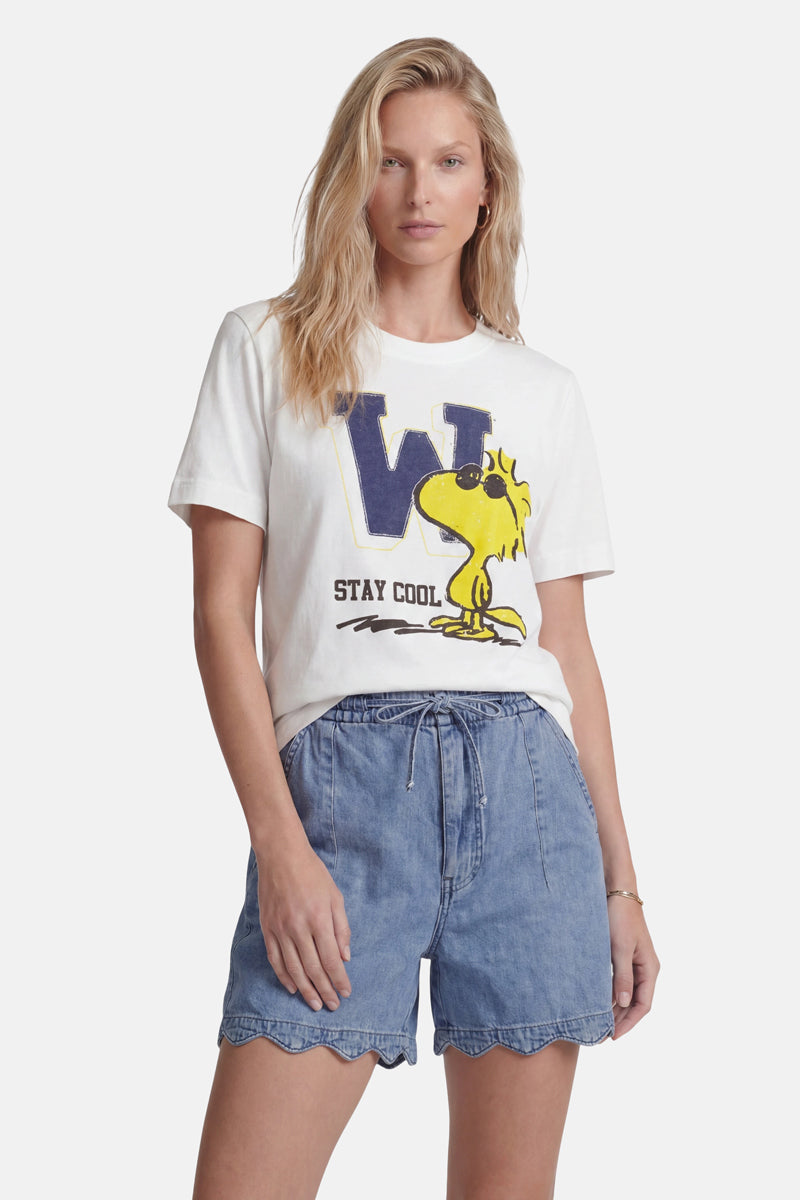 Eine Frau mit langen blonden Haaren trägt ein „Princess Goes Hollywood“-T-Shirt aus Baumwolle in limitierter Auflage mit einem großen blauen „W“, einem Woodstock-Aufdruck und dem Schriftzug „STAY COOL“, dazu hellblaue Shorts mit hoch tailliertem, gewelltem Saum vor einem schlichten weißen Hintergrund.