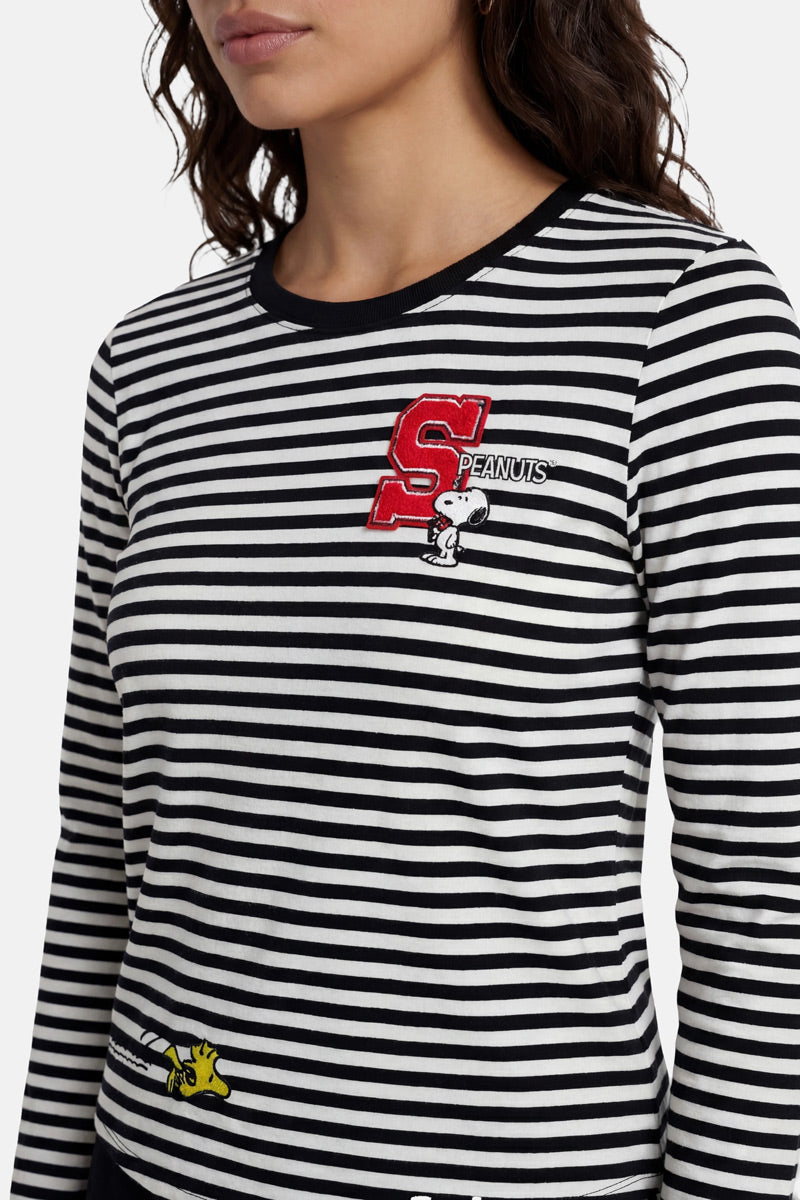 Eine Frau trägt ein gestreiftes Langarmshirt der Marke „Princess Goes Hollywood“ mit den Aufdrucken „S“ und „Peanuts“, einer Snoopy-Stickerei im Brustbereich und einem kleinen gelben Woodstock, der in Höhe der Taille aufgestickt ist. Zu sehen sind nur ihr Oberkörper und der untere Teil ihres Gesichts.