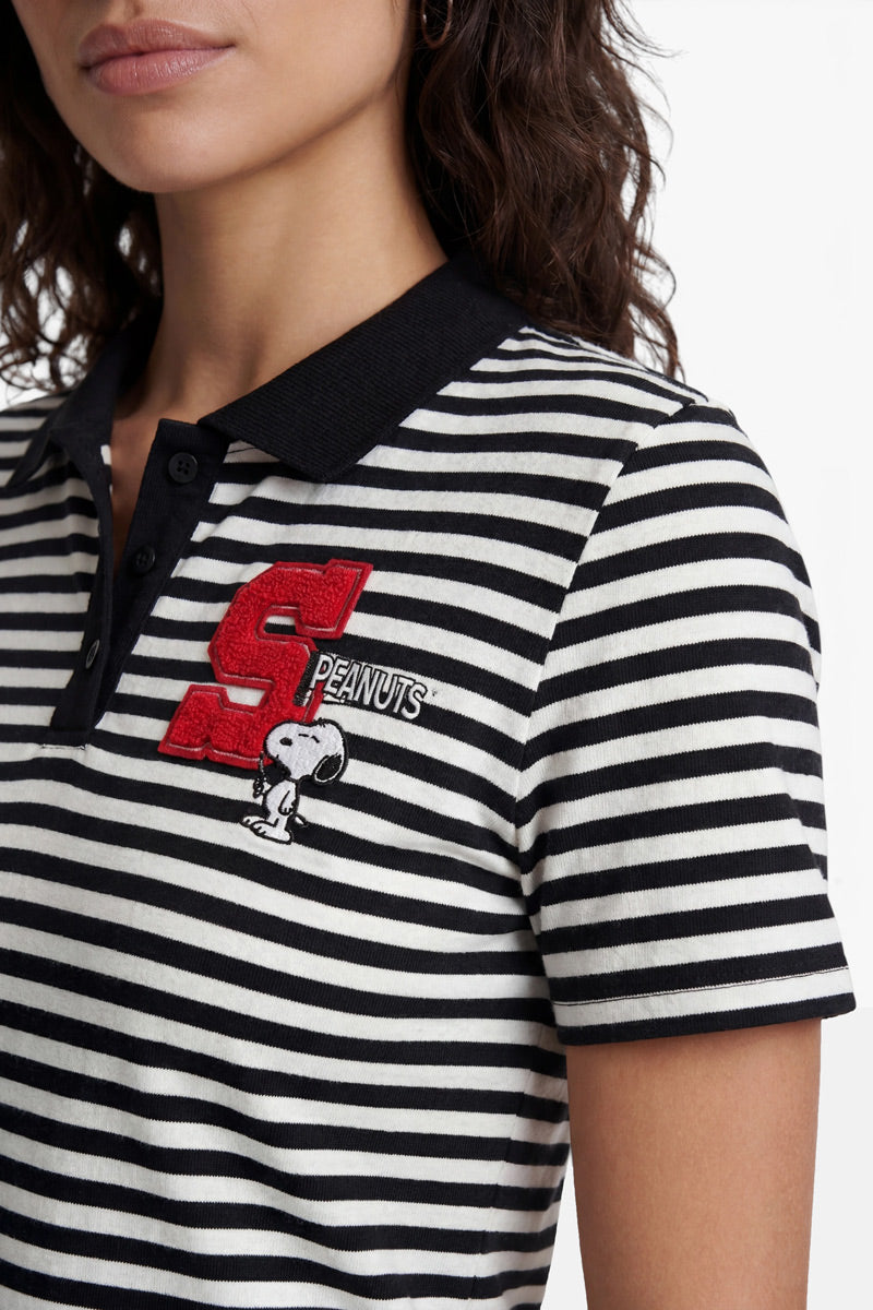 Eine Frau trägt ein gestreiftes „Princess Goes Hollywood“-T-Shirt mit schwarzem Kragen, einem auffälligen roten „S“-Aufnäher, dem Schriftzug „Peanuts“ und einer Snoopy-Stickerei auf der Brust. Vor dem weißen Hintergrund sind nur ihr Kopf und ihr Oberkörper zu sehen.