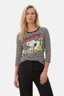 Eine Frau mit welligem blondem Haar trägt ein „Princess Goes Hollywood Limited Edition Snoopy“-Shirt – ein schwarz-weiß gestreiftes Oberteil mit 3/4-Ärmeln, auf dem Snoopy und Woodstock abgebildet sind, sowie den roten Schriftzug „Snoopy“ – und eine schwarze Hose. Sie steht selbstbewusst vor einem schlichten Hintergrund.