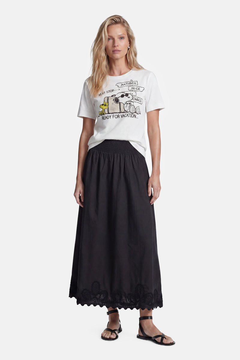 Eine Frau mit langen blonden Haaren trägt ein weißes „Princess Goes Hollywood“-Snoopy-T-Shirt aus Baumwolle und einen schwarzen, hoch taillierten, knöchellangen Rock mit Wellenrand. Sie steht in schwarzen Sandalen vor einem schlichten weißen Hintergrund. Limitierte Auflage.