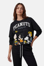 Eine Frau mit mittellangem braunem Haar trägt einen Pullover aus der „Princess Goes Hollywood“-Limited-Edition-Kollektion zu „Peanuts“, auf dem Charlie Brown, Lucy, Snoopy, Woodstock und Sally abgebildet sind, zusammen mit dem Schriftzug „PEANUTS Running Club“. Sie steht vor einem hellgrauen Hintergrund.