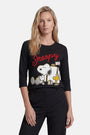 Eine Frau mit langen blonden Haaren trägt ein Langarmshirt aus Baumwolle der Limited Edition „Princess Goes Hollywood“ mit großen Cartoon-Motiven von Snoopy und Woodstock, über denen in roter Schreibschrift „Snoopy“ steht; sie blickt nach vorne und hat eine Hand in der Tasche.