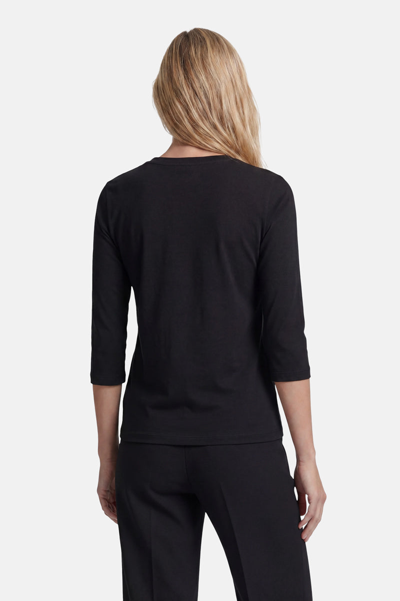 Eine Person mit langen, welligen blonden Haaren ist von hinten zu sehen. Sie trägt ein eng anliegendes schwarzes Langarmshirt von „Princess Goes Hollywood“ und eine schwarze Hose. Der schlichte weiße Hintergrund hebt das Outfit hervor, während die Person mit entspannt an den Seiten hängenden Armen dasteht.