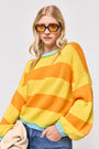 Eine Frau mit langen blonden Haaren trägt eine orangefarbene Sonnenbrille und einen Princess Goes Hollywood gestreifter Pullover mit Baumwolleanteil mit breiten gelben und orangefarbenen Streifen, Rundhalsausschnitt, blauer Verzierung, Blue Jeans und hält einen beigen Mantel.