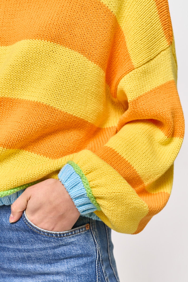 Eine Person modelliert einen Princess Goes Hollywood gestreifter Pullover mit blauem und grünem Besatz an den Ärmelbündchen und einem klassischen Rundhalsausschnitt, gepaart mit einer blauen Jeans. Der einfarbige Hintergrund hebt nur ihren Oberkörper und einen Teil eines Arms hervor.