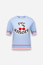 Der pastellblaue Princess Goes Hollywood Per Amore Pullover zeigt den Schriftzug "per amore" in fetter schwarzer Schrift mit zwei roten Kirschen zwischen den Wörtern sowie rot-weiß gestreifte Borten an den Ärmeln und am Saum vor einem schlichten hellen Hintergrund.