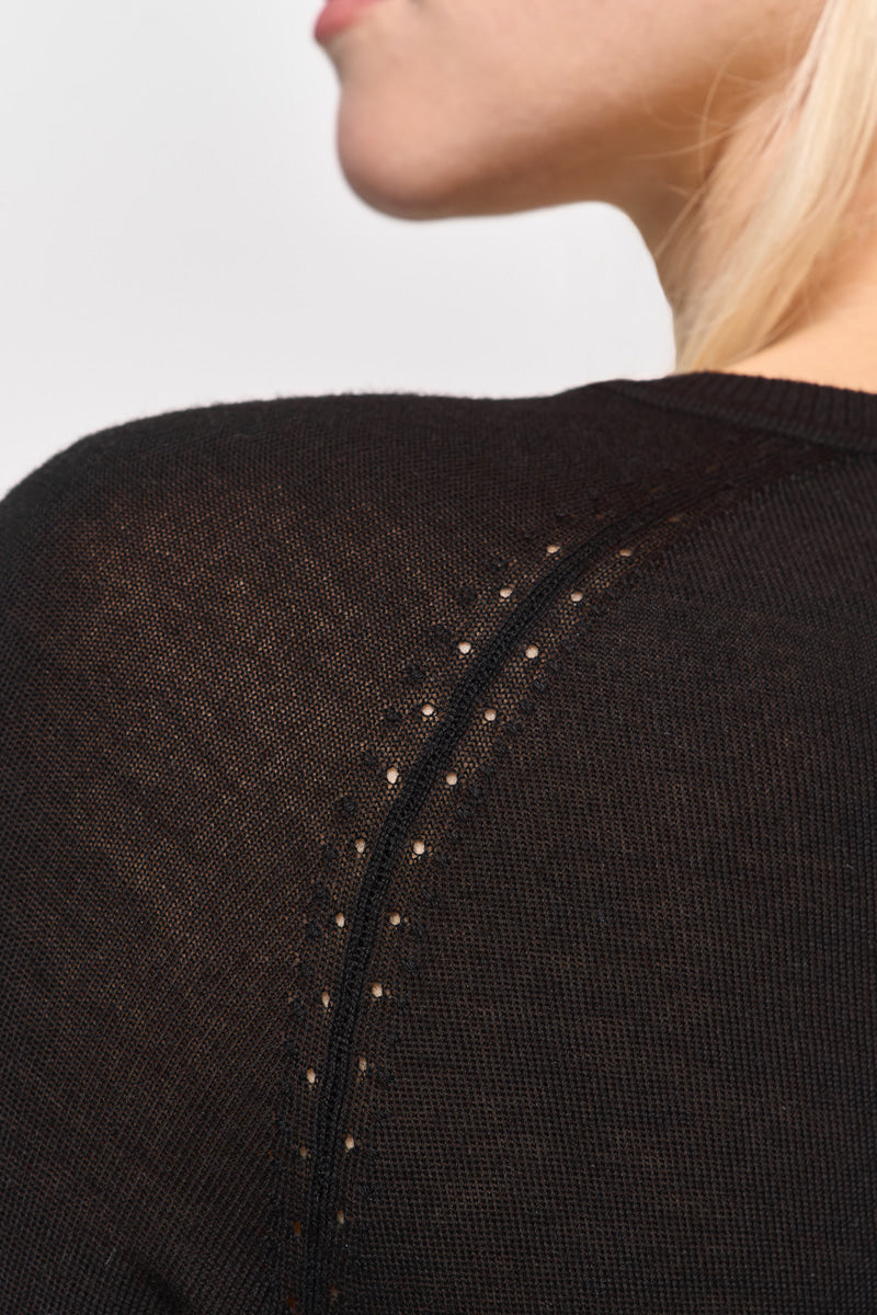 Nahaufnahme einer Person, die einen schwarzen Strickpullover mit Raglanärmeln von Princess Goes Hollywood trägt, wobei die dezenten diagonalen perforierten Details an der Schulter hervorgehoben werden. Hellblondes Haar ist teilweise sichtbar; das Gesicht ist größtenteils außerhalb des Rahmens.