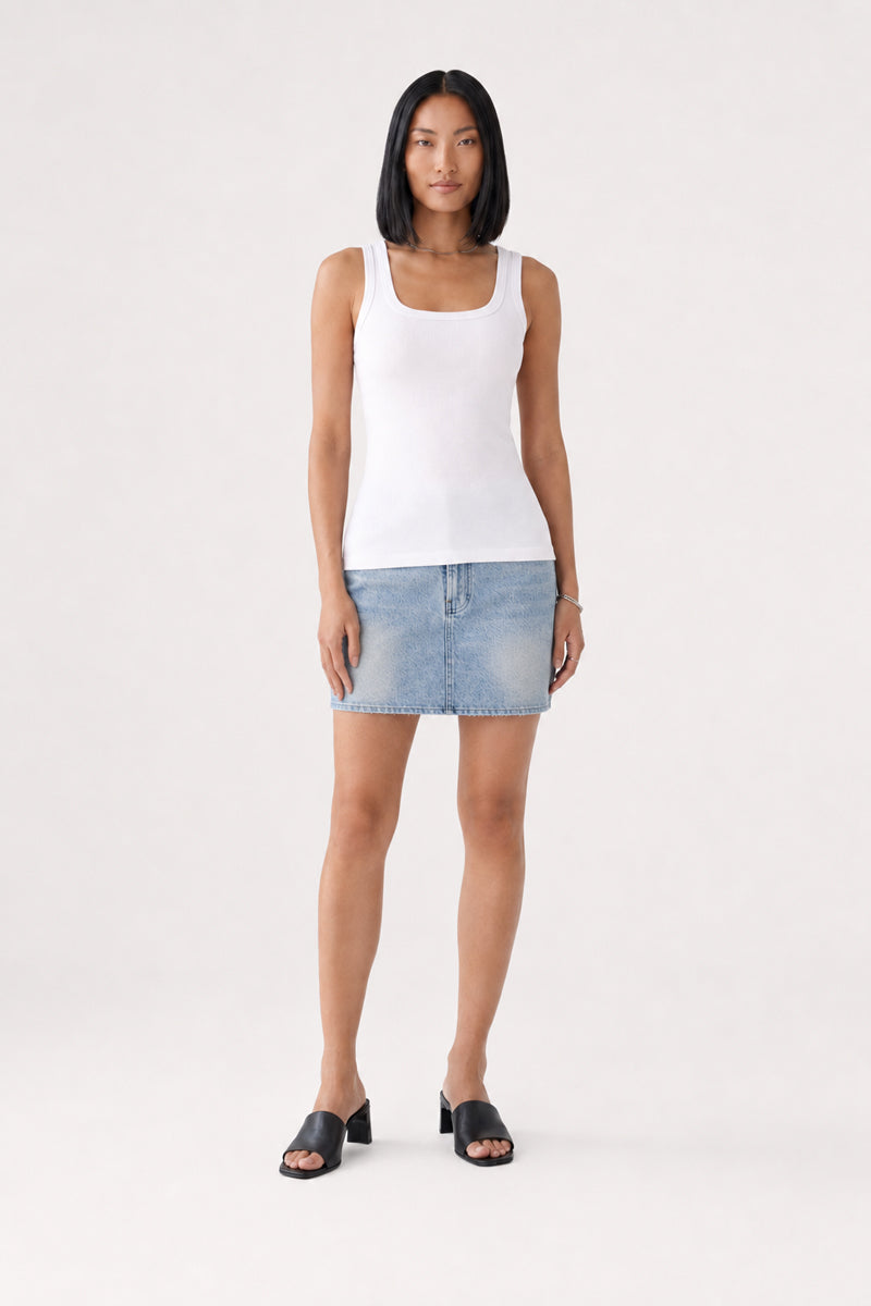Eine Frau mit glattem schwarzem Haar trägt ein weißes, ärmelloses Basic-Top mit Rundhalsausschnitt von Princess Goes Hollywood, dazu einen hellblauen Jeans-Minirock und schwarze Pantoletten mit offener Spitze und Absatz. Sie steht mit dem Blick nach vorne vor einem schlichten hellen Hintergrund, die Arme entspannt an den Seiten.