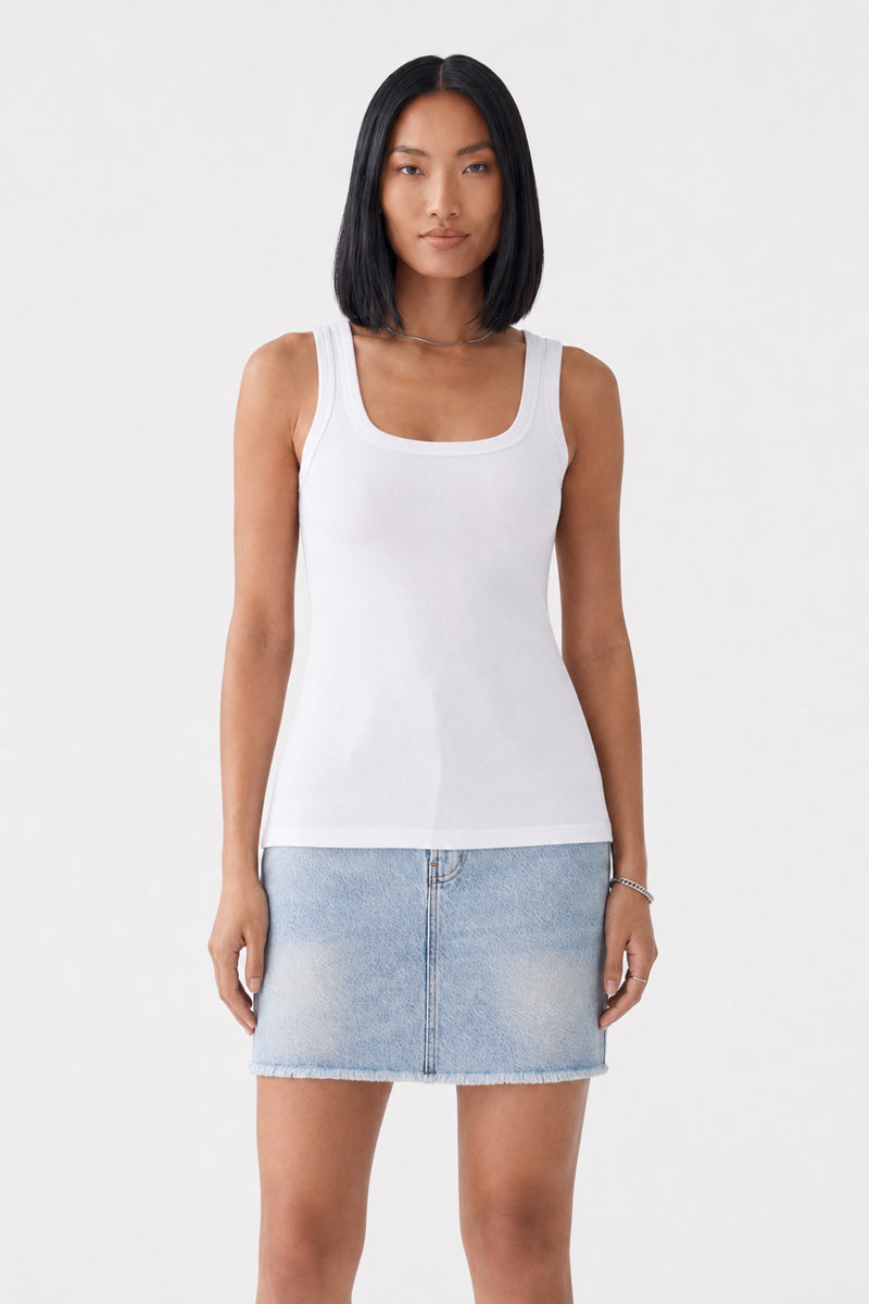 Eine Frau mit glattem, schulterlangem schwarzem Haar trägt ein eng anliegendes weißes „Princess Goes Hollywood Basic Top“ aus Baumwolle mit Rundhalsausschnitt und einen hellblauen Jeans-Minirock. Sie steht mit dem Blick nach vorne vor einem schlichten hellen Hintergrund, die Arme entspannt an den Seiten.