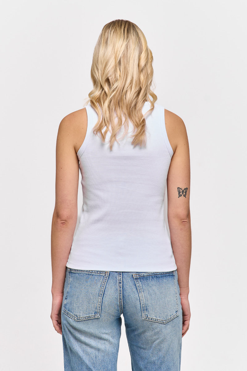 Eine Frau mit gewelltem blondem Haar, von hinten gesehen, trägt ein einfaches weißes Princess Goes Hollywood Baumwolle-Top mit Rundhalsausschnitt und hellblaue Jeans. Sie hat ein kleines schwarzes Schmetterlingstattoo auf dem linken Oberarm; der Hintergrund ist schlicht weiß.