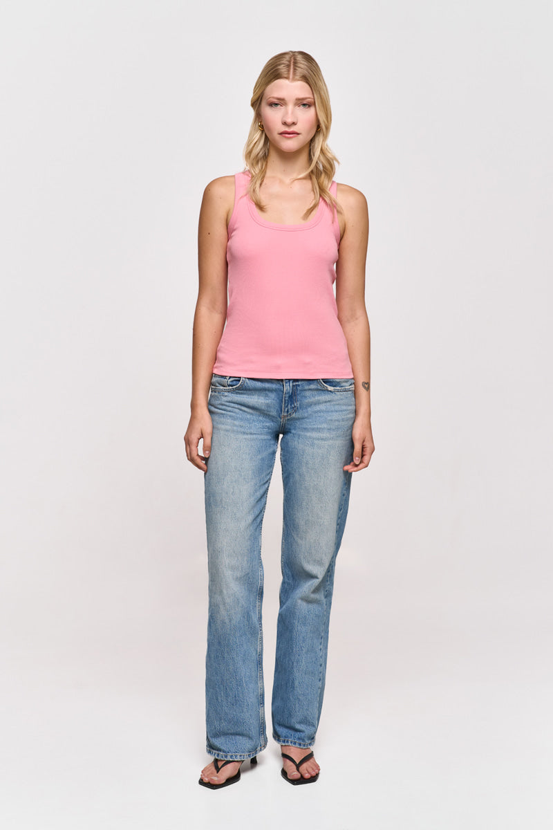 Eine Frau mit heller Haut und langen blonden Haaren steht mit dem Gesicht nach vorne vor einem weißen Hintergrund. Sie trägt ein rosa Princess Goes Hollywood Basic Top aus Baumwolle mit Rundhalsausschnitt, blaue Jeans und schwarze Flip-Flops.