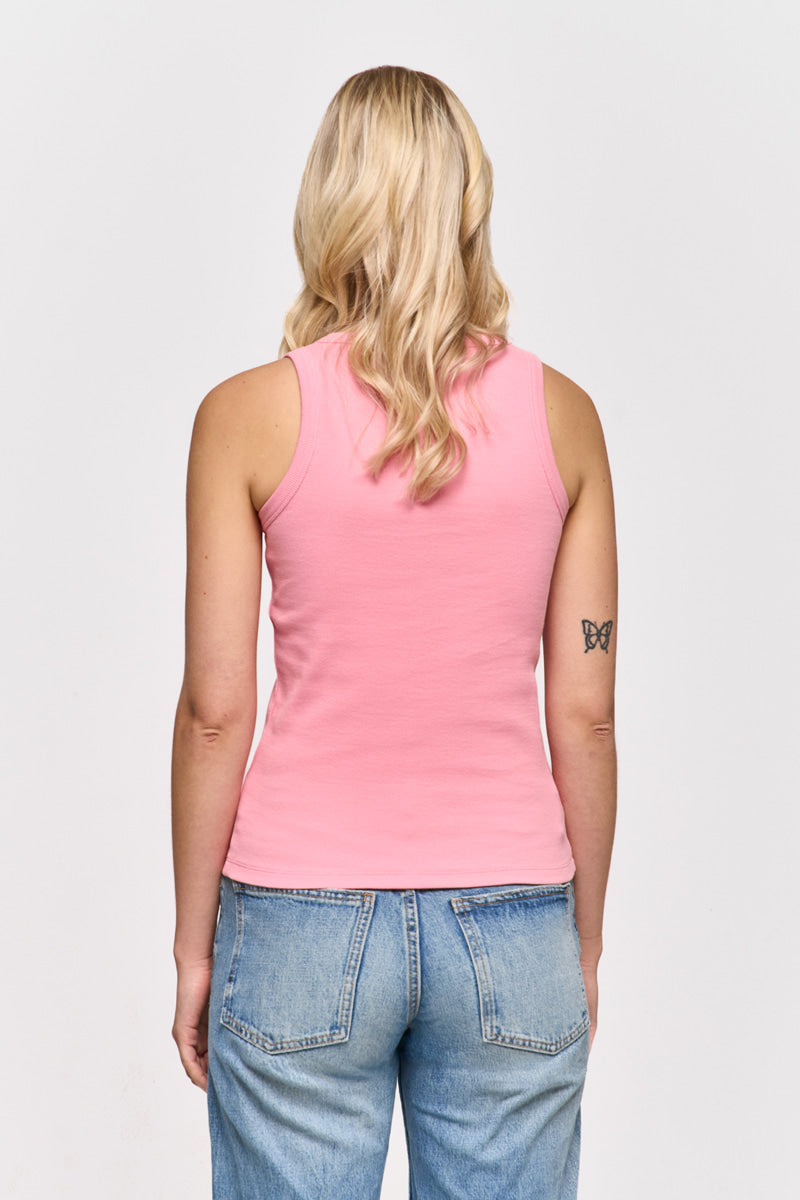 Eine Frau mit gewelltem blondem Haar, von hinten gesehen, trägt ein ärmelloses rosa Princess Goes Hollywood Basic Top aus Baumwolle und hellblaue Jeans. Auf ihrem linken Oberarm befindet sich ein kleines Schmetterlingstattoo vor weißem Hintergrund.
