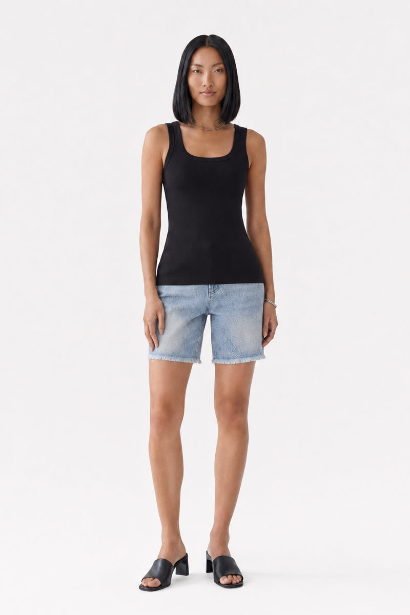 Eine Frau mit glattem schwarzem Haar, die ein geripptes Basic-Top der Marke „Princess Goes Hollywood“ mit Rundhalsausschnitt in Schwarz, knielange Shorts aus hellblauem Denim und schwarze Sandalen mit offener Zehenpartie trägt, steht mit dem Blick nach vorne vor einem schlichten weißen Hintergrund. Ihre Arme liegen ganz natürlich an den Seiten. Das Top ist aus weicher Baumwolle gefertigt und eignet sich daher ideal für den bequemen Alltag.