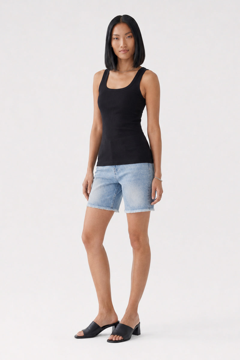 Eine Frau mit glattem schwarzem Haar trägt ein eng anliegendes, geripptes Basic-Top mit Rundhalsausschnitt aus schwarzer Baumwolle von „Princess Goes Hollywood“, hellblaue Jeans-Bermudashorts und schwarze Sandalen mit offener Zehenpartie und Absatz. Sie steht mit dem Blick nach vorne vor einem schlichten weißen Hintergrund, die Arme entspannt an den Seiten.