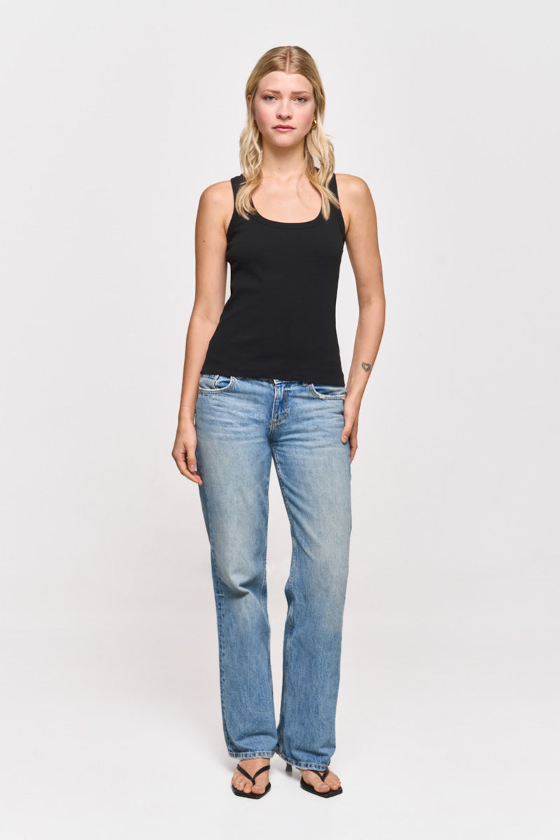 Eine Frau mit langen blonden Haaren steht mit dem Gesicht nach vorne vor einem weißen Hintergrund. Sie trägt ein schwarzes Baumwolloberteil mit Rundhalsausschnitt von Princess Goes Hollywood, hellblaue Jeans mit geradem Bein und schwarze Flip-Flops. Ihre Arme ruhen natürlich an ihren Seiten.
