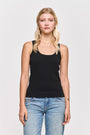Eine Frau mit langen blonden Haaren steht vor einem weißen Hintergrund und trägt ein schwarzes Princess Goes Hollywood Basic Top mit Rundhalsausschnitt aus Baumwolle und hellblaue Jeans. Ihre Arme sind entspannt, und auf ihrem linken Unterarm ist ein kleines Herz-Tattoo zu sehen.