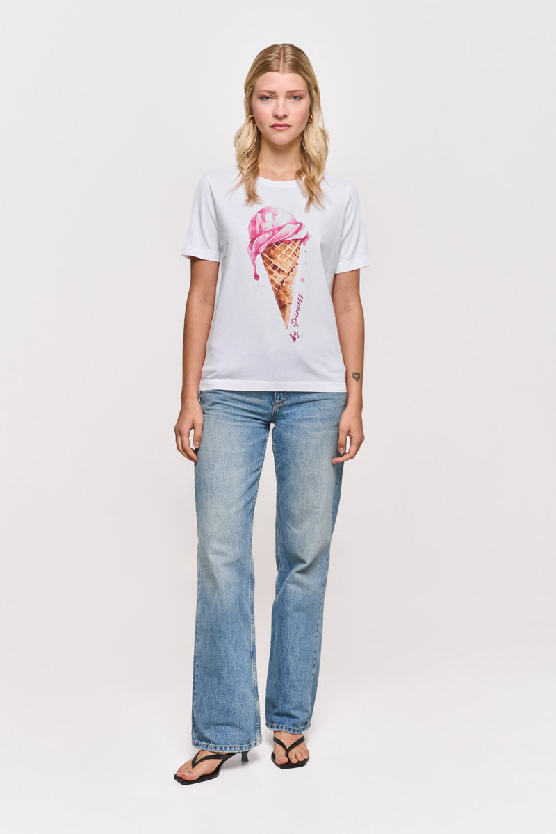 Eine Frau mit blondem Haar und neutralem Gesichtsausdruck blickt vor einem weißen Hintergrund nach vorne. Sie trägt eine blaue Jeans und ein Princess Goes Hollywood T-Shirt aus weißer Baumwolle mit pinkem Eis-Print, Strassstein-Akzenten und schwarzen Flip Flops.