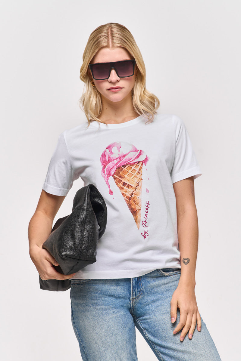 Eine blonde Frau trägt eine große Sonnenbrille und ein "Princess Goes Hollywood"-Baumwoll-T-Shirt mit einer Grafik einer schmelzenden rosa Eistüte, gepaart mit einer blauen Jeans. Sie trägt eine schwarze Jacke, auf der ein kleines Herz-Tattoo auf ihrem Handgelenk zu sehen ist, vor einem schlichten weißen Hintergrund.
