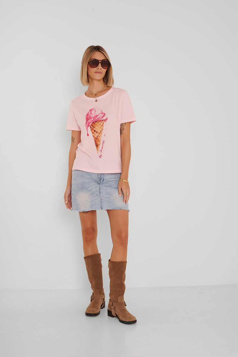 Eine Frau mit Bob-Haarschnitt und Sonnenbrille trägt ein rosa Baumwoll-T-Shirt mit Eiscreme-Aufdruck, einen hellblauen Jeans-Minirock und hohe braune Wildlederstiefel vor einem schlichten weißen Hintergrund.