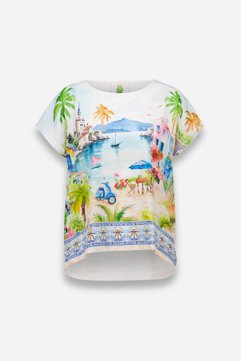 Eine kurzärmelige weiße Bluse von Princess Goes Hollywood aus luftiger Baumwolle mit einem lebhaften Positano-Print mit Palmen, Booten, einem Leuchtturm, pastellfarbenen Gebäuden, einem Motorroller, Strandkörben und blau gemusterten Bordüren.