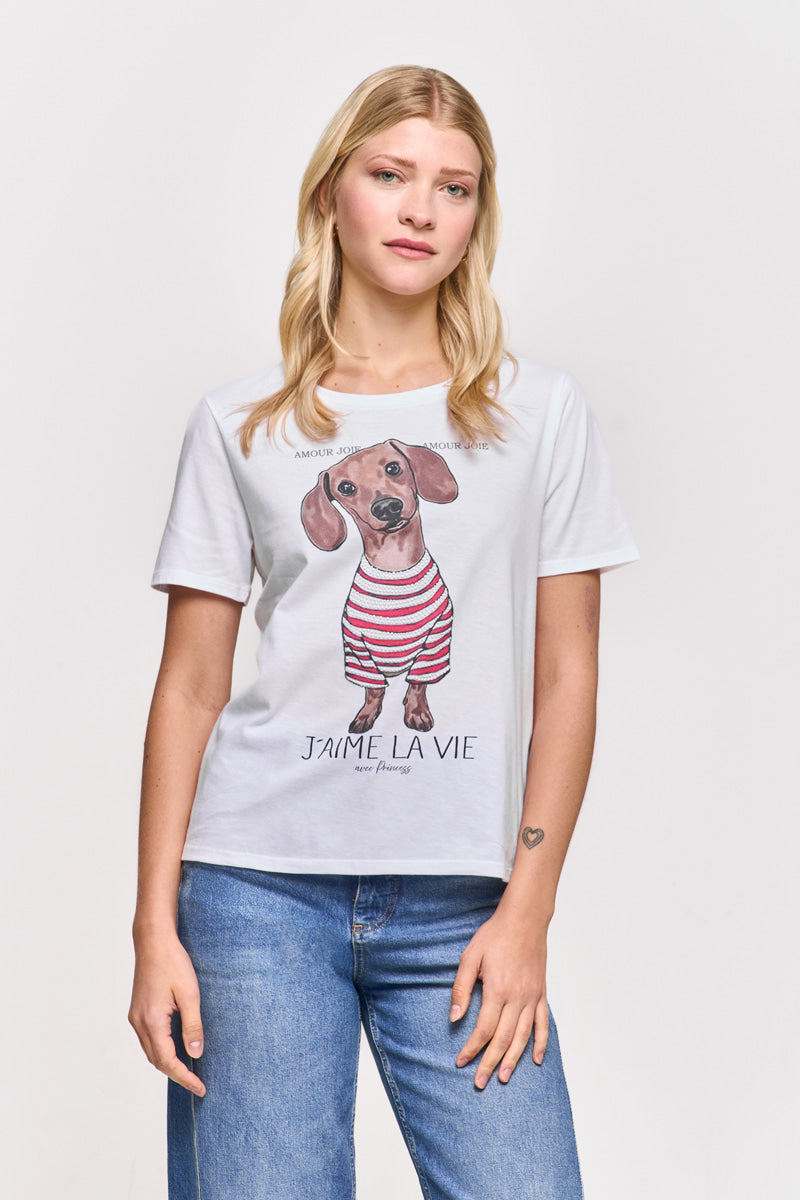 Eine blonde Frau modelliert ein Princess Goes Hollywood Baumwolle T-Shirt mit einem illustrierten Dackel in roten und weißen Streifen, französischem Text und Dackel-Print. Dazu trägt sie eine blaue Jeans und zeigt ein kleines Herz-Tattoo auf ihrem linken Handgelenk.