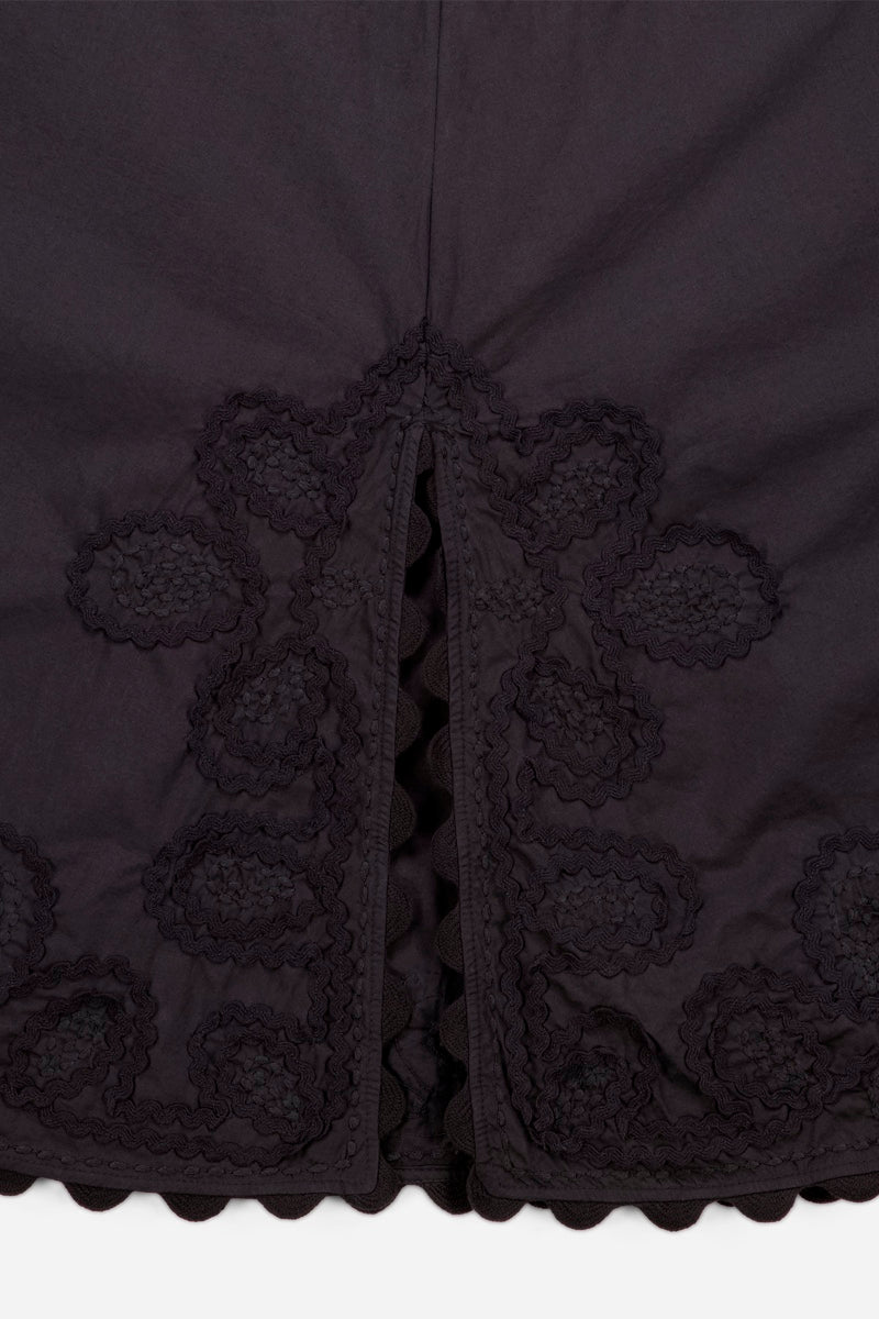Nahaufnahme des schwarzen Princess Goes Hollywood Baumwolle Midikleid-Stoffes mit einem zentralen Schlitz, der mit einer Wellenkante eingefasst ist. Der Schlitz und der Saum sind mit floralen Stickereimustern verziert, die ebenfalls mit Wellenkanten verziert sind und für zusätzliche Details sorgen.