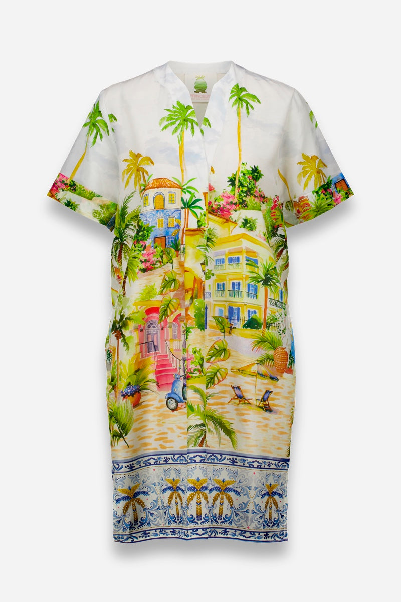 Das knielange, kurzärmelige Blusenkleid von Princess Goes Hollywood aus einem Baumwoll-Seiden-Gemisch zeigt einen farbenfrohen Positano-Aufdruck - Palmen, Häuser, roter Motorroller und Sonnenliegen - auf weißem Grund mit einer blau-goldenen Zierborte.