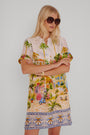 Eine Frau mit langen blonden Haaren trägt eine große dunkle Sonnenbrille und ein buntes Positano-Print Blusenkleid von Princess Goes Hollywood aus einem Baumwoll-Seiden-Gemisch. Sie steht mit verschränkten Armen vor einem schlichten weißen Hintergrund und schaut leicht zur Seite.