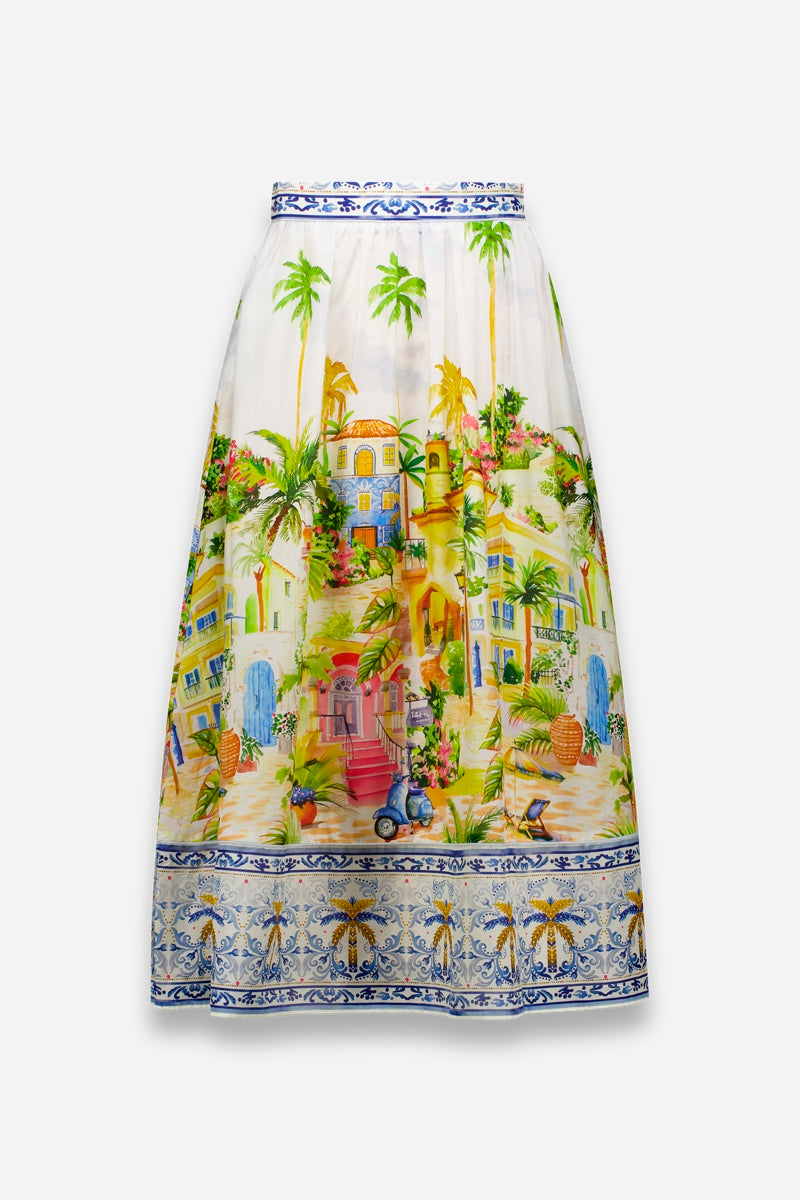 Princess Goes Hollywood präsentiert einen farbenfrohen, knielangen Midirock mit einem lebhaften Positano-Print aus Palmen, Häusern und Kopfsteinpflaster. Er ist aus einem luxuriösen Baumwoll-Seiden-Gemisch gefertigt und verfügt über blaue Blumenborten am Saum und an der Taille.