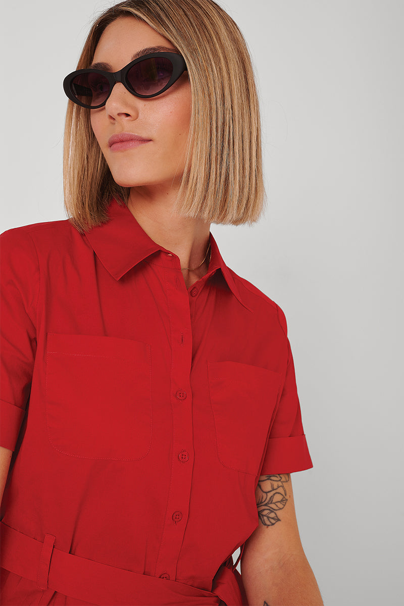 Eine Frau mit glattem, schulterlangem blondem Haar trägt eine schwarze Cat-Eye-Sonnenbrille und ein rotes Midi-Hemdkleid aus Baumwollpopeline mit Brusttaschen von Princess Goes Hollywood und steht vor einem schlichten hellgrauen Hintergrund.