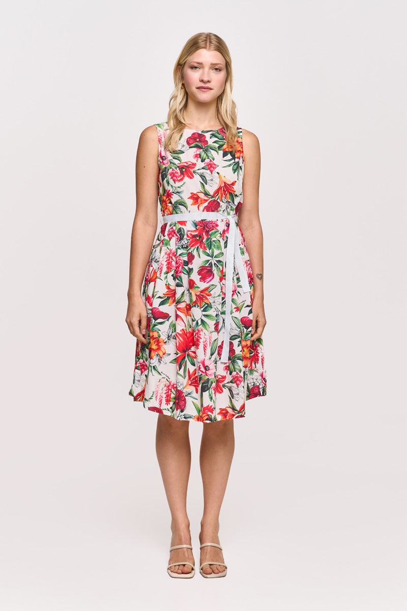 Eine Frau mit langen blonden Haaren trägt ein ärmelloses, knielanges Princess Goes Hollywood Baumwolle Minikleid mit einem auffälligen roten, grünen und rosa Blumenprint. Dazu trägt sie nackte Riemchensandalen vor einem schlichten weißen Hintergrund.