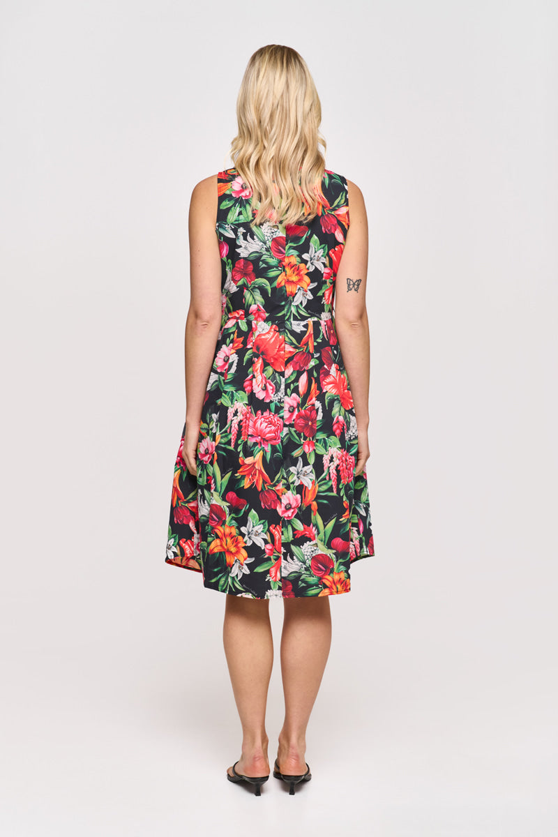 Eine Frau mit welligem blonden Haar trägt ein ärmelloses Minikleid von Princess Goes Hollywood aus Baumwolle mit buntem Blumenprint in Rot, Pink und Grün. Sie steht in Sandalen vor weißem Hintergrund und hat ein Schmetterlingstattoo am linken Arm.