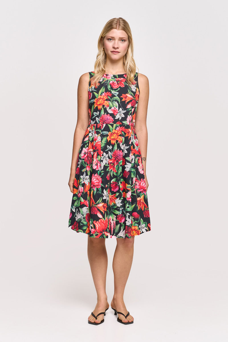 Eine Frau mit lockeren blonden Haaren und neutralem Gesichtsausdruck trägt ein ärmelloses schwarzes Baumwollminikleid mit einem bunten Blumenmuster in Rot, Pink und Grün von Princess Goes Hollywood, gepaart mit schwarzen Flip-Flops vor weißem Hintergrund.