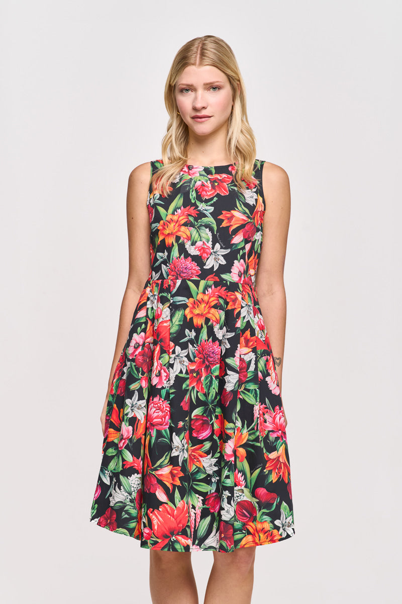 Eine blonde Frau trägt ein ärmelloses schwarzes Princess Goes Hollywood Baumwolle Minikleid mit einem lebhaften Blumendruck in Rot, Orange, Gelb, Rosa und grünen Blättern. Sie steht mit dem Gesicht nach vorne vor einem schlichten hellen Hintergrund.