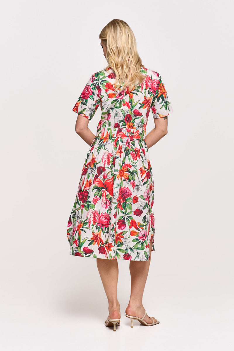 Eine Frau mit blonden, welligen Haaren trägt ein weißes Midikleid mit buntem Blumenprint in Rot, Pink und Grün von Princess Goes Hollywood und beigefarbenen Heels. Der Hintergrund ist schlicht weiß.