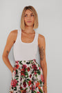 Eine Frau mit blondem Bob trägt ein weißes Basic-Top aus Baumwolle mit Rundhalsausschnitt von Princess Goes Hollywood und einen hoch taillierten geblümten Rock. Florale Tattoos und goldener Schmuck sind sichtbar, sie blickt neutral zur Seite.