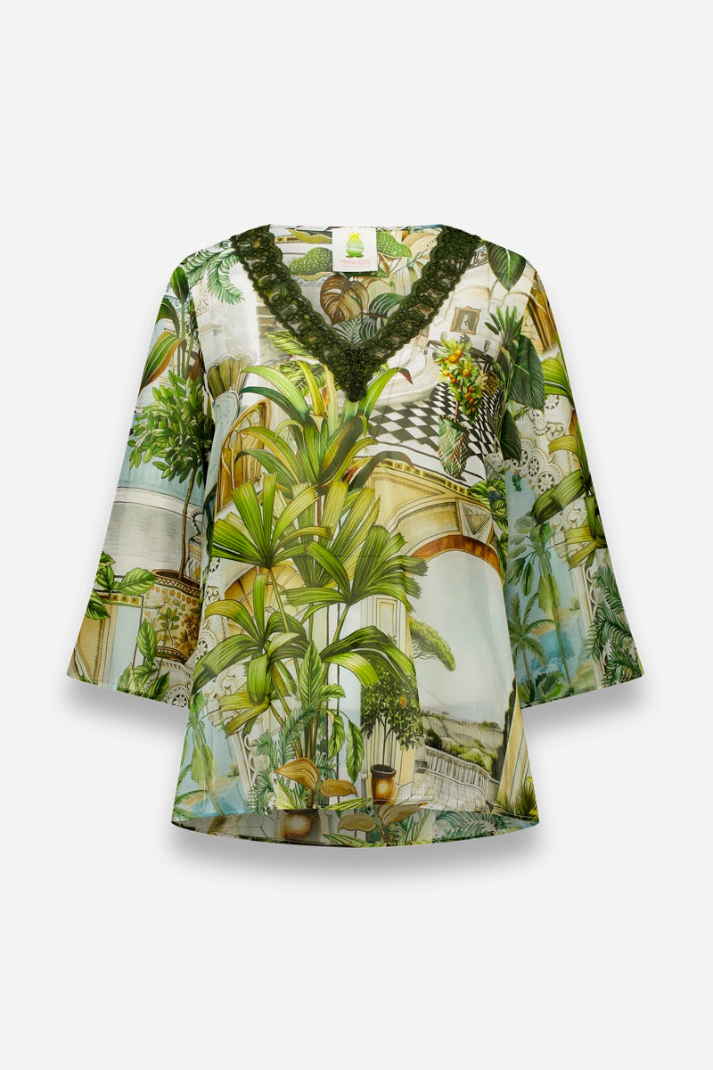 Die locker sitzende Seidenbluse von Princess Goes Hollywood hat Dreiviertelärmel, einen V-Ausschnitt mit dunkelgrüner Spitze und einen leuchtenden Safaridruck mit üppigen Pflanzen und architektonischen Motiven auf einem strahlend weißen Hintergrund in Erdtönen.